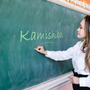 Nauczycielka zapisuje na tablicy słowo Kamishibai.