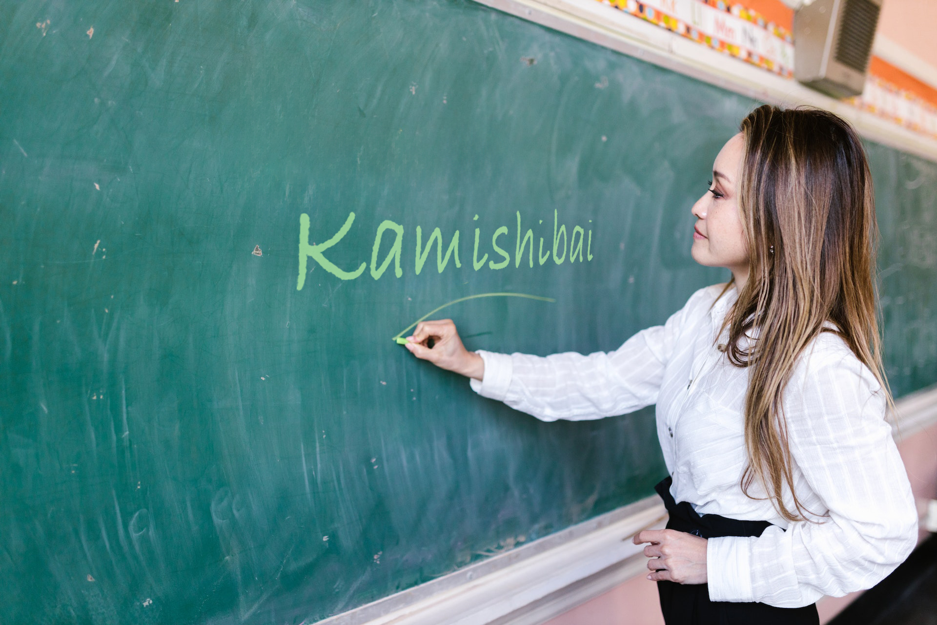 Nauczycielka zapisuje na tablicy słowo Kamishibai.